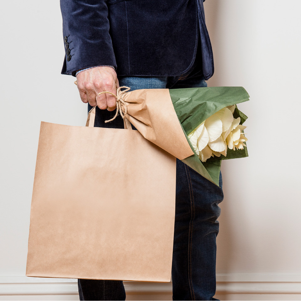 Man holding paper carry bag and bunch of flowers.