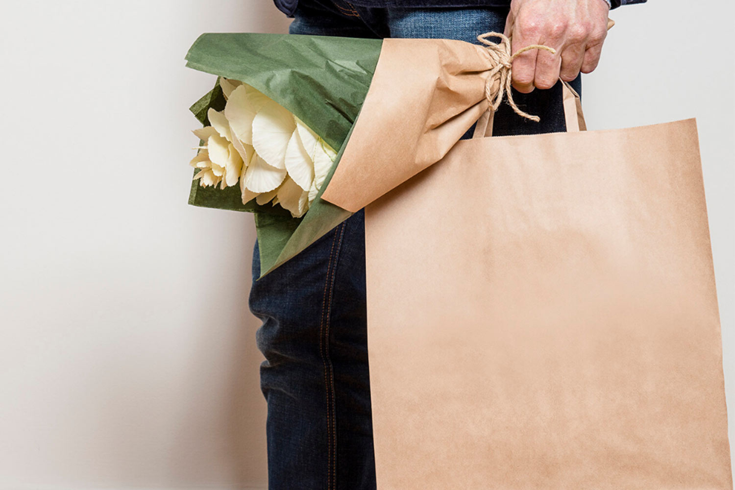 Man holding bouquet of flowers and a kraft paper gift bag.
